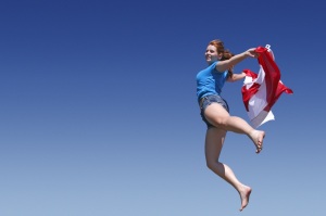 Girl jumping with the Canadian flag against backdrop of blue sky