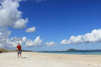 Karikari beach Northland New Zealand blue skies white sand and a man in a red top throwing a rugby ball