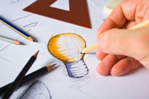 Photo showing a hand sketching a lightbulb surrounded by pencils